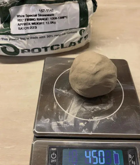 A ball of light brown clay sits on a digital scale displaying 450g, with a bag of Potclay White Special Stoneware in the background.